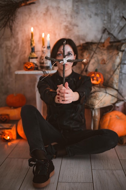 Woman on the background of festive Halloween decorations with a wooden cross