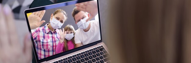 Woman in background waving hand into laptop screen with image of man, woman and little girl