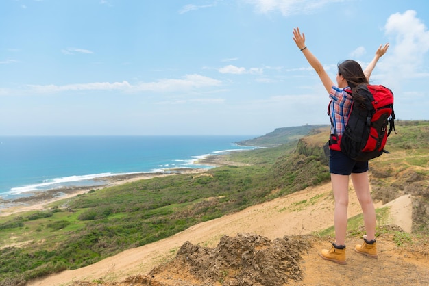 woman backpacker visiting the famous hiking mountain and face to the sea scenery open hands enjoying the natural wind and blue sky.