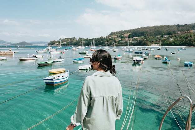 Woman backwards in front of the sea with a lot of boats during a sunny day