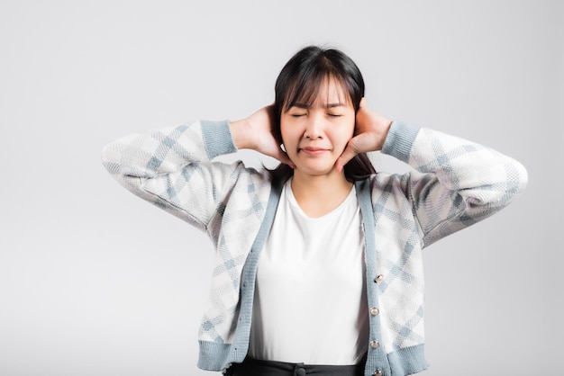 Woman bad mood pain her closed ears with hand palms and close eyes, Asian beautiful young female covers ears for loud noise, studio shot isolated on white background with copy space