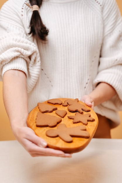 Woman baker in a white sweater holding a wooden board with gingerbread cookies