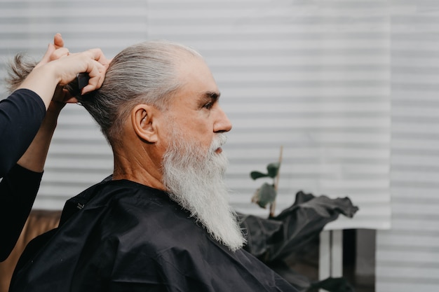 Woman barber cutting hair to an aged bearded man