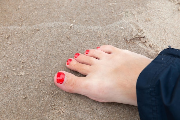 Woman bare feet with red nail polish on the sand, close up