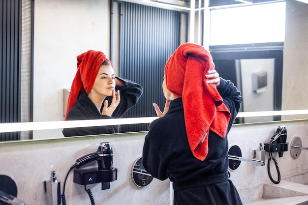 A woman in a bathrobe is looking in a mirror and brushing her hair.