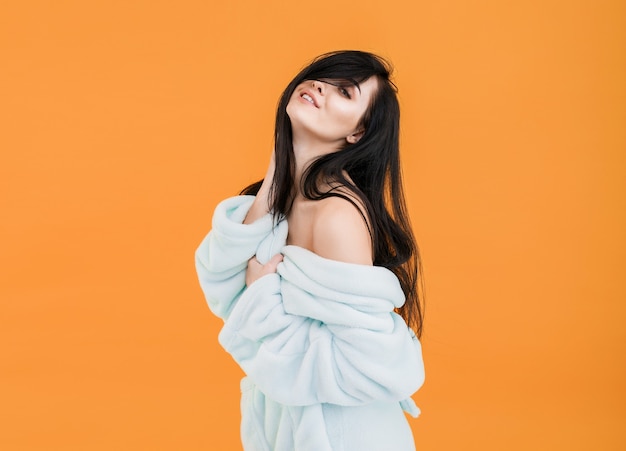 woman in bathrobe with bare shoulders posing on orange background