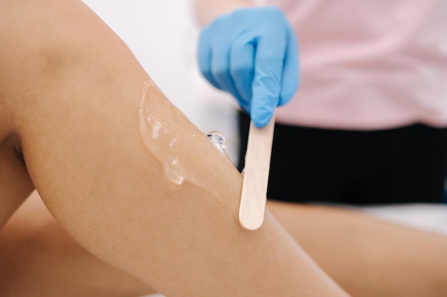 Woman beautician in blue glowes applies contact gel on the leg of a woman for laser hair removal in cosmetology studio Close up