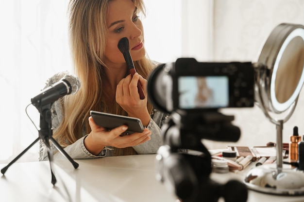 Woman beauty blogger applying blush powder on her face during video recording for her followers