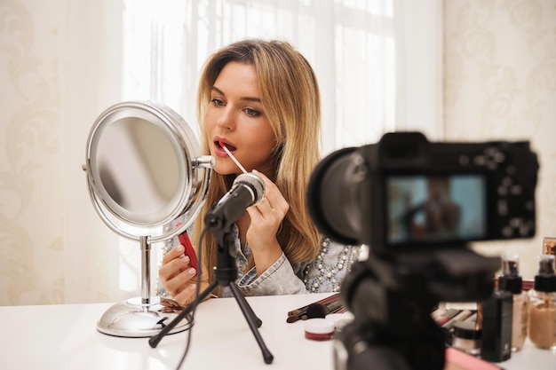 Woman beauty blogger applying lipstick on her lips during video recording for her followers