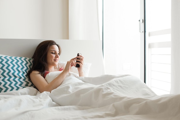 Woman in bed checking social apps with smartphone