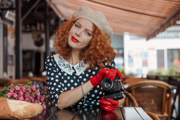 A woman in a beret and vintage dress holds a camera in her hands and takes shoots