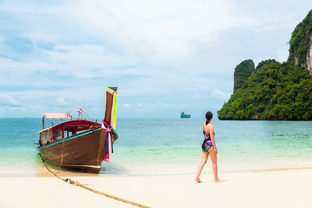 Woman in bikini walking on the beach with long tail boat in tropical island.