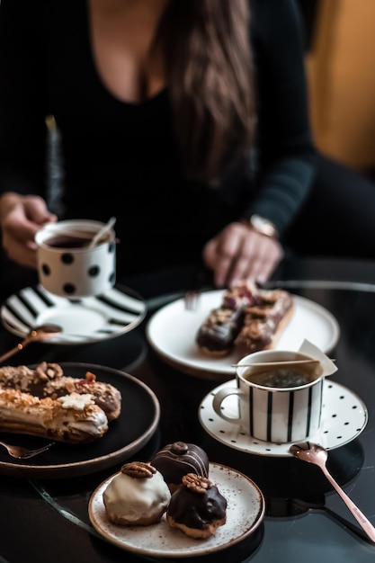 A woman in a black dress in a cafe or restaurant drinks tea and eats Traditional French dessert eclairs or profiteroles