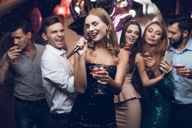 A woman in a black dress is singing songs with her friends.