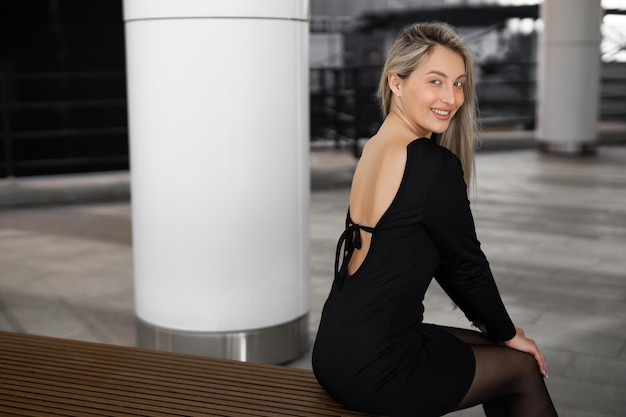 A woman in a black dress sits on a bench in front of a white column.