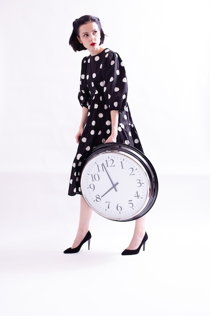 woman in a black evening dress with white polka dots holding a clock