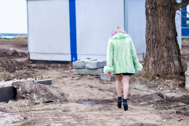 A woman in black fishnet tights and heeled ankle boots walks along a path