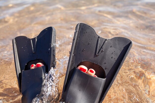 A woman in black flippers splashes near the shore. Fins stick out of the water. Swimming equipment.