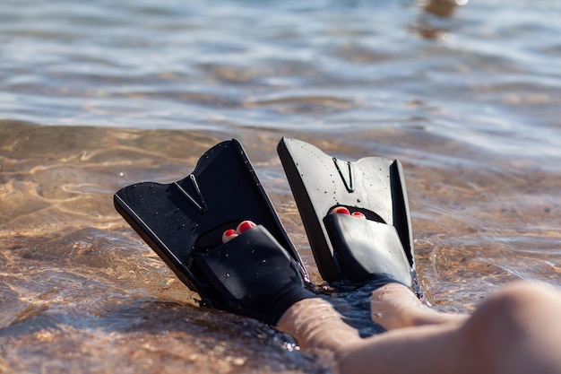 A woman in black flippers splashes near the shore. Fins stick out of the water. Swimming equipment