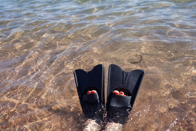 A woman in black flippers splashes near the shore. Fins stick out of the water. Swimming equipment