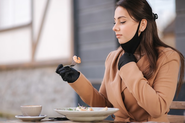 Woman in black gloves hold cutlery. Quarantine Cafe concept. Food outdoors in protective gloves.