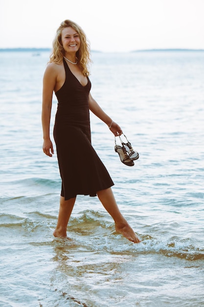 Woman in black light dress walking barefoot by sea beach