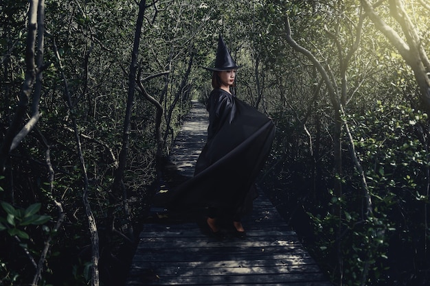 Woman in Black Scary witch halloween costume with moonlight in a dark forest