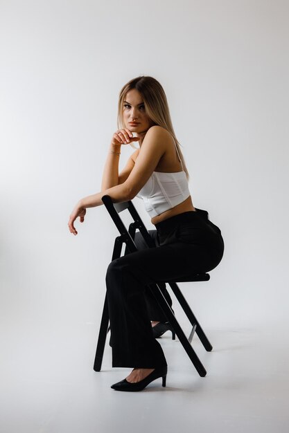 A woman in a black shirt and white pants sits on a white cube