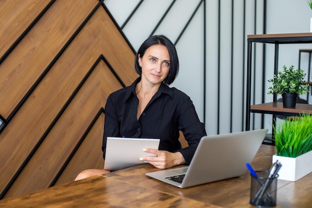 A woman in a black shirt with a notebook near a laptop at a meeting