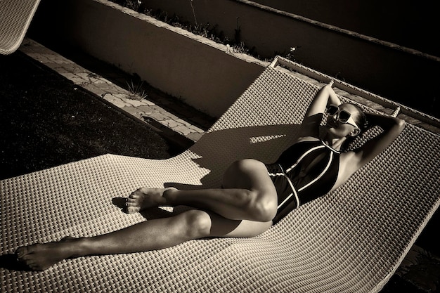 Woman in a black swimsuit and white sunglasses sunbathing on a sunbed