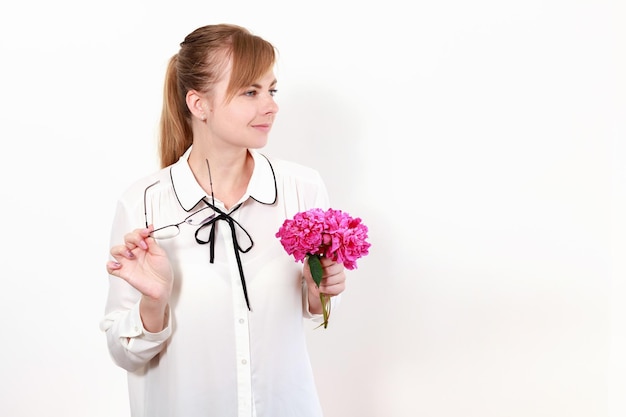 A woman in a blouse with peonies in her hand looks away banner