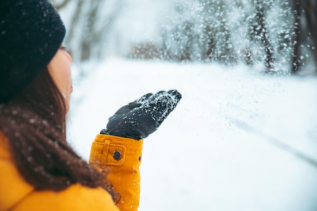 Woman blowing snow from her hands snowed park on background winter season