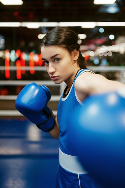 Woman in blue boxing gloves hits, box training on ring. Female boxer in gym, kickboxing sparring in sport club, girl kickboxer workout