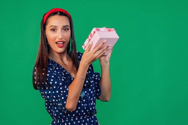 Woman in a blue dress holding a gift box near her ear and liste