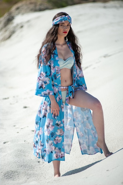 A woman in a blue floral kimono stands on the sand.