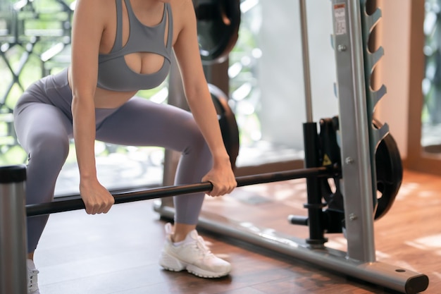 Woman in blue sportswear exercises lifting bar at gym