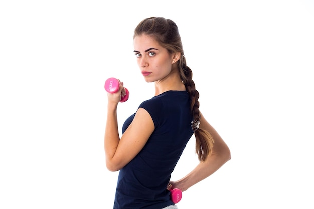 Woman in blue Tshirt and gray shorts standing back and holding pink dumbbells in her hands