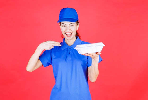 Woman in blue uniform holding a white plastic takeaway box for delivery. 