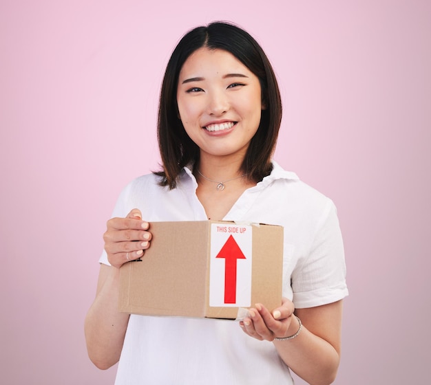 Woman box and delivery courier and e commerce with portrait and package isolated on pink background Asian customer commercial and supply chain with shipping parcel and export service in studio