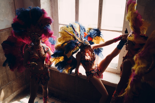 Woman in brazilian samba carnival costume with colorful feathers plumage relax in old entrance with big window.