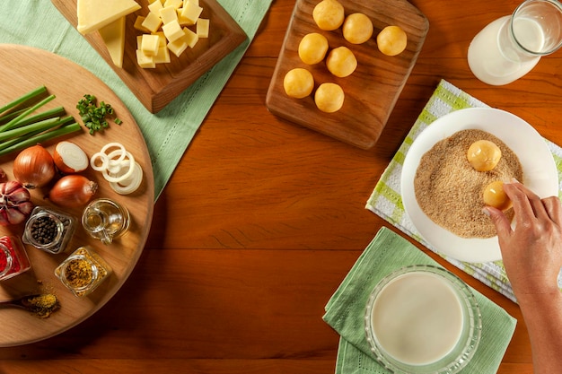 Woman breading brazilian cheese stuffed croquette bolinha de queijo on a wooden table Top view