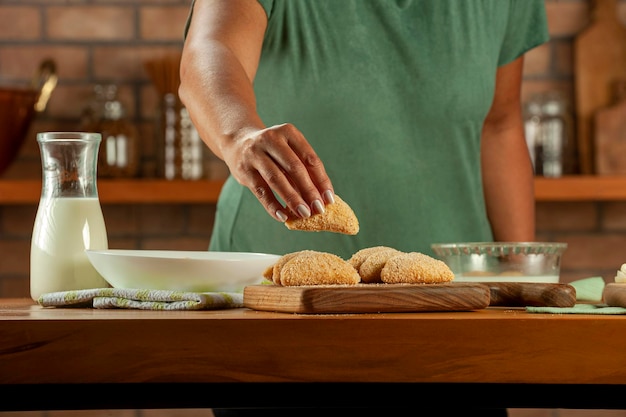 Woman breading brazilian meat stuffed croquette risolis de carne on a wooden table Top view