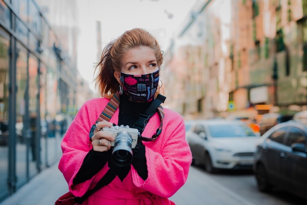 Woman in a bright pink coat is a tourist with a camera in a stylish glamorous fashionable protective...