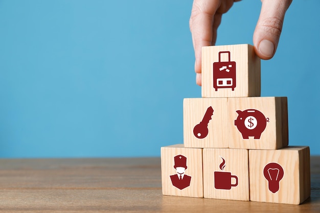 Woman building pyramid of cubes with different icons on wooden table against light blue background closeup Insurance concept