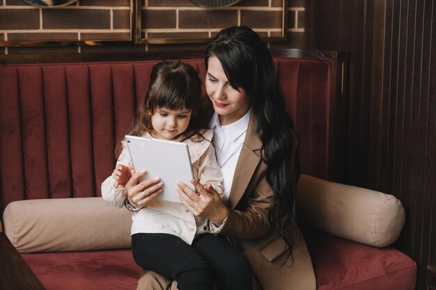 A woman in a business suit holds her child in her arms and speaks via video link on a tablet