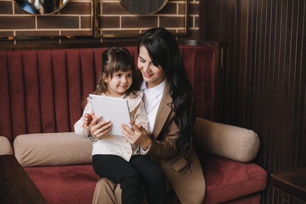 A woman in a business suit holds her child in her arms and speaks via video link on a tablet