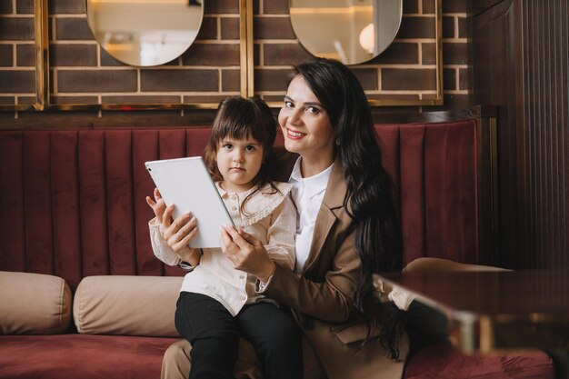 A woman in a business suit holds her child in her arms and speaks via video link on a tablet