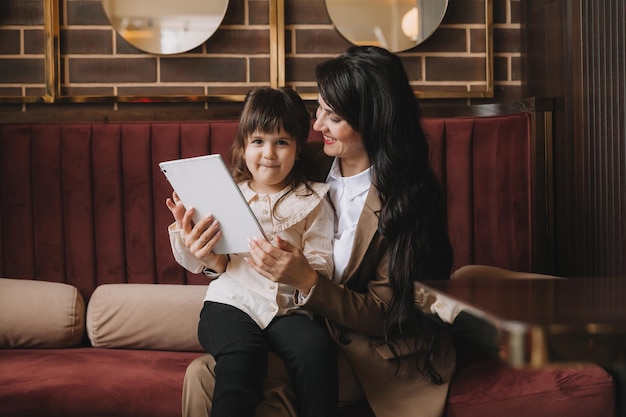 A woman in a business suit holds her child in her arms and speaks via video link on a tablet