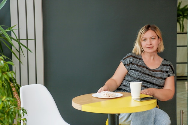 woman in a cafe drinks coffee in a paper cup and eats cake