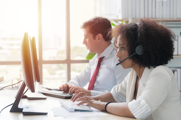 Woman call center African American wearing white work clothes with headset working in call center at computer